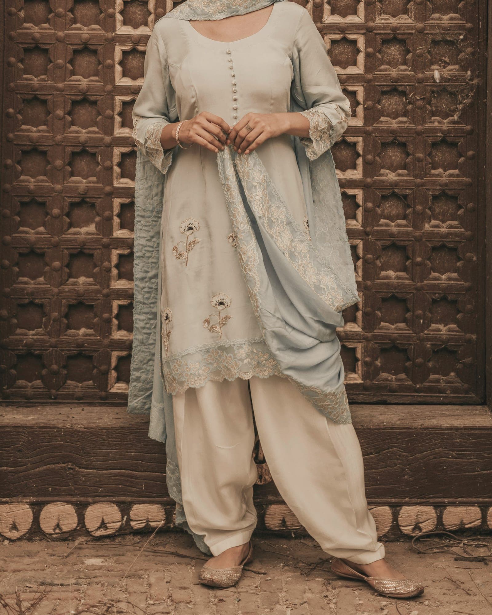 A powder-blue embroidered kurta, salwar and lace-edged dupatta in front of a carved wooden door