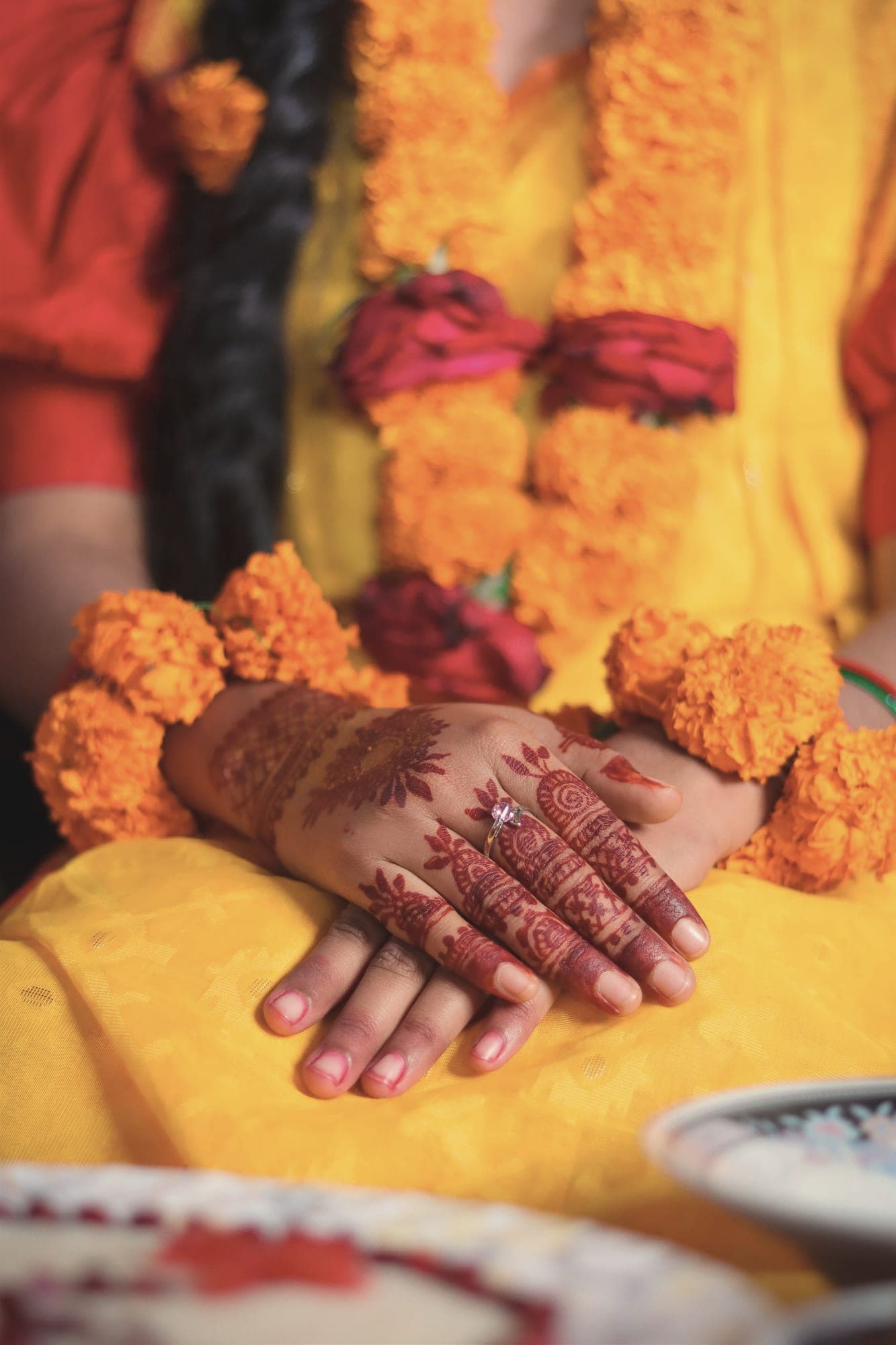 Hennaed hands resting on mustard-yellow fabric with marigold garlands